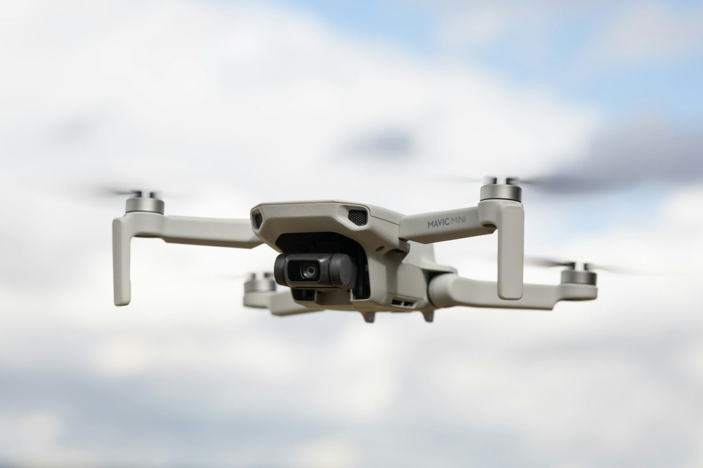 A drone hovering in the air against a cloudy sky.